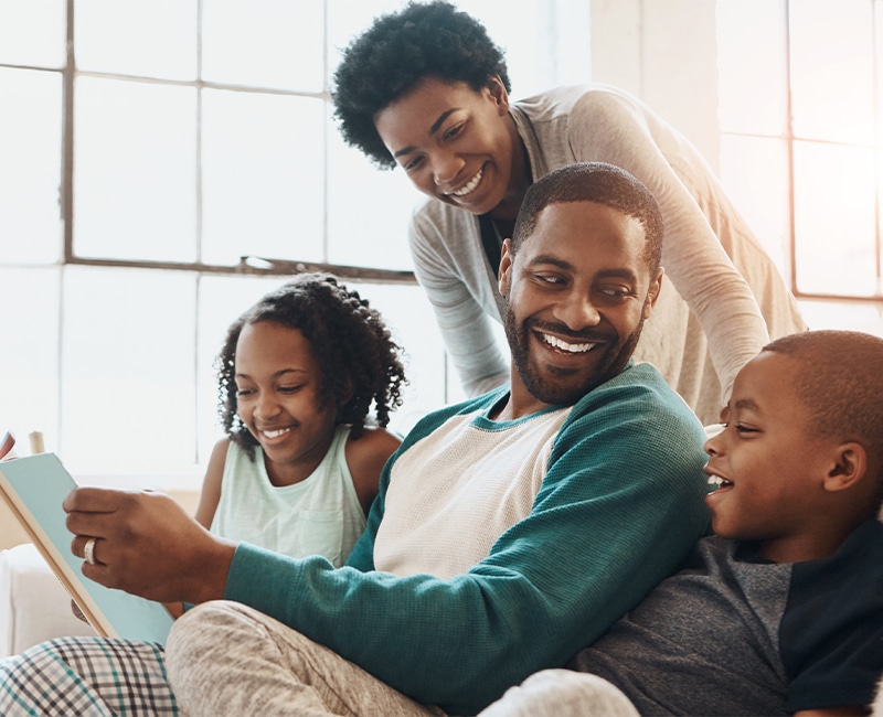 Reading, happy and black family with book on sofa for bonding together on fathers day at home