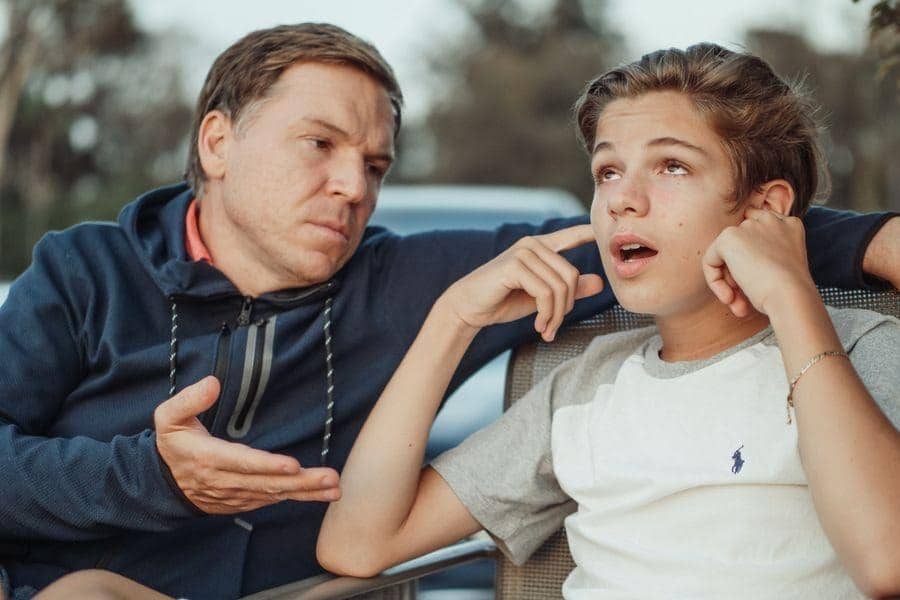 An adult and a teenager talking outdoors.