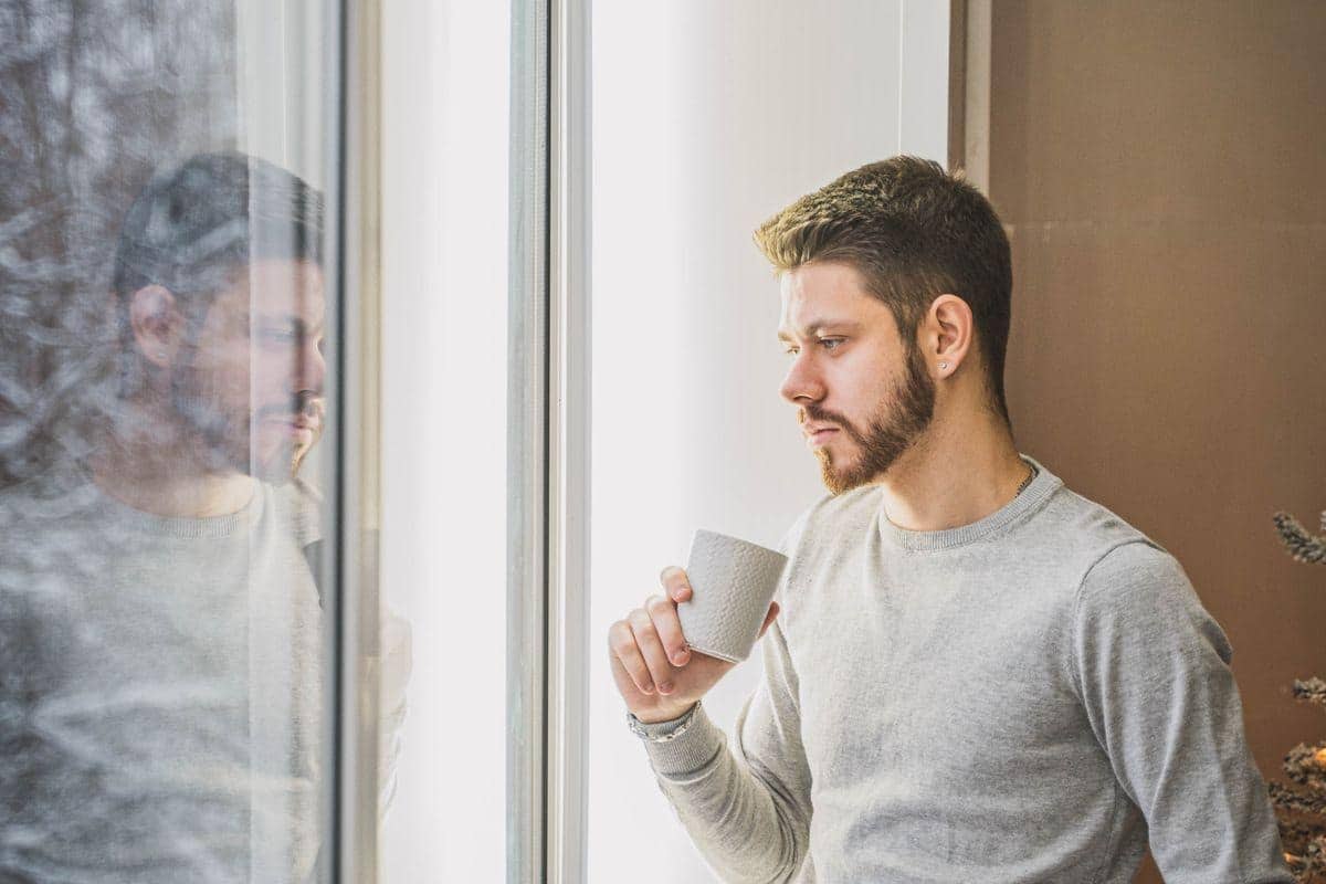 Man holding a mug while looking out a window